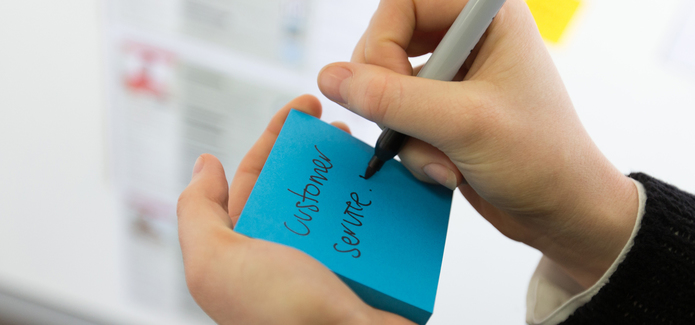 Hand writing Customer Service on a blue post it