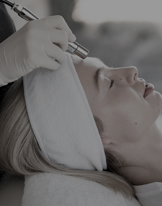 Clinician performing a facial treatment on a reclining client