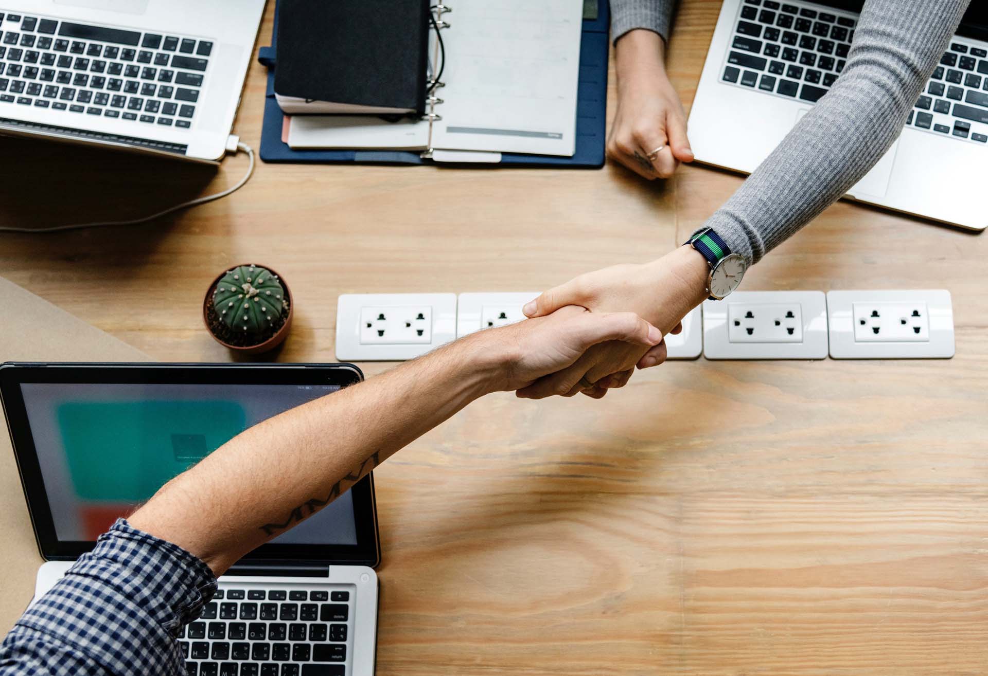 Two people shaking hands over work desk