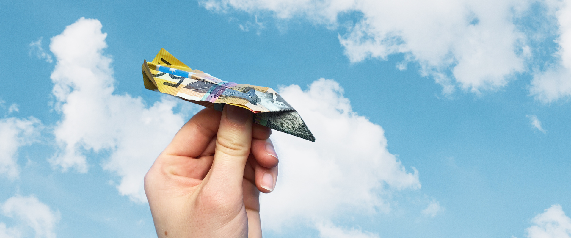 A hand holding an AU$50 banknote paper aeroplane against a blue sky