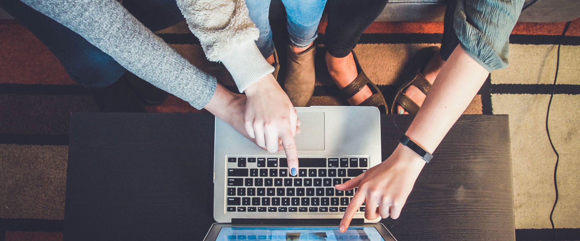 Overhead image of a three young people pointing at a laptop screen