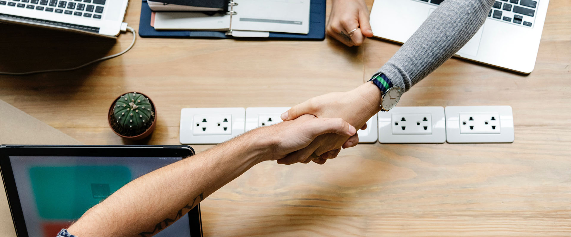 Two people shaking hands over work desk